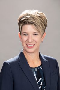 A blonde, white woman is smiling in a professional headshot. She has short hair.